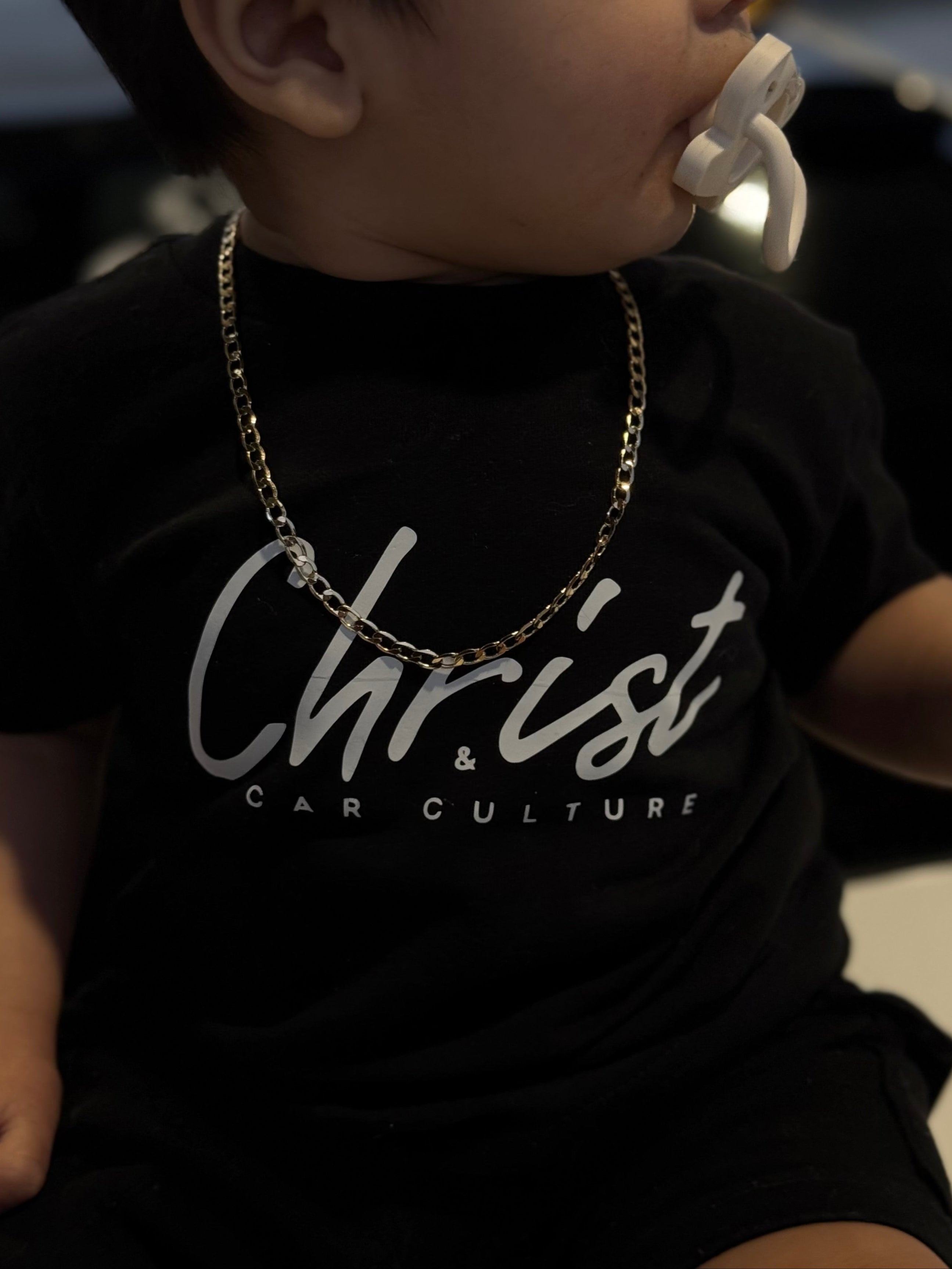 Child wearing a black t-shirt with 'Christ & Car Culture' text and a gold chain.